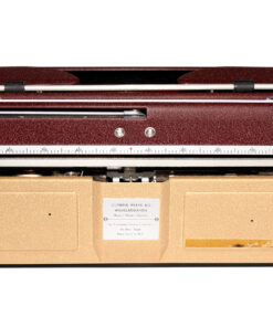 Vintage red-brown manual typewriter resting on a beige carrying case, with visible carriage, ruler scale, and metal components.