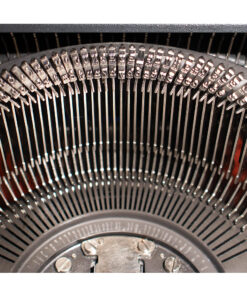 Close-up of a circular arc of metal pins or teeth inside a vintage mechanical device, forming a comb-like pattern in metallic gray. The dense arrangement suggests an internal mechanism or print/typewriting component.