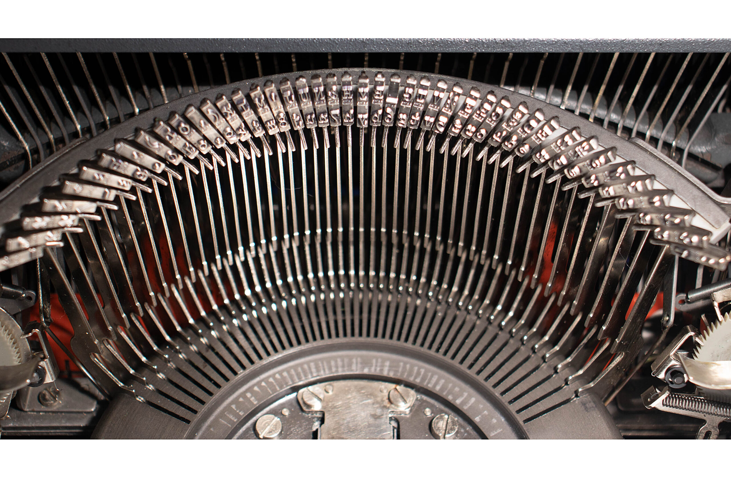 Close-up of a circular arc of metal pins or teeth inside a vintage mechanical device, forming a comb-like pattern in metallic gray. The dense arrangement suggests an internal mechanism or print/typewriting component.