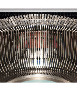 Close-up of a vintage typewriter's metal type bars forming a curved arc across the frame, ready to strike inked letters to paper.