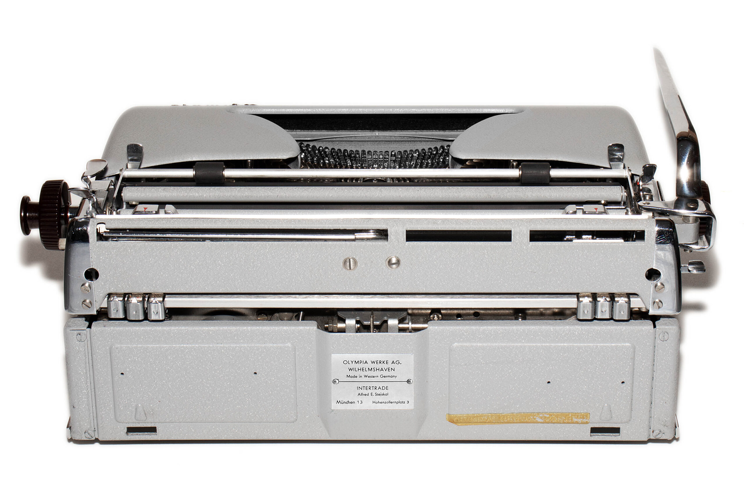 Rear view of a gray vintage Olympia typewriter with exposed type mechanism and a small label on the back plate.