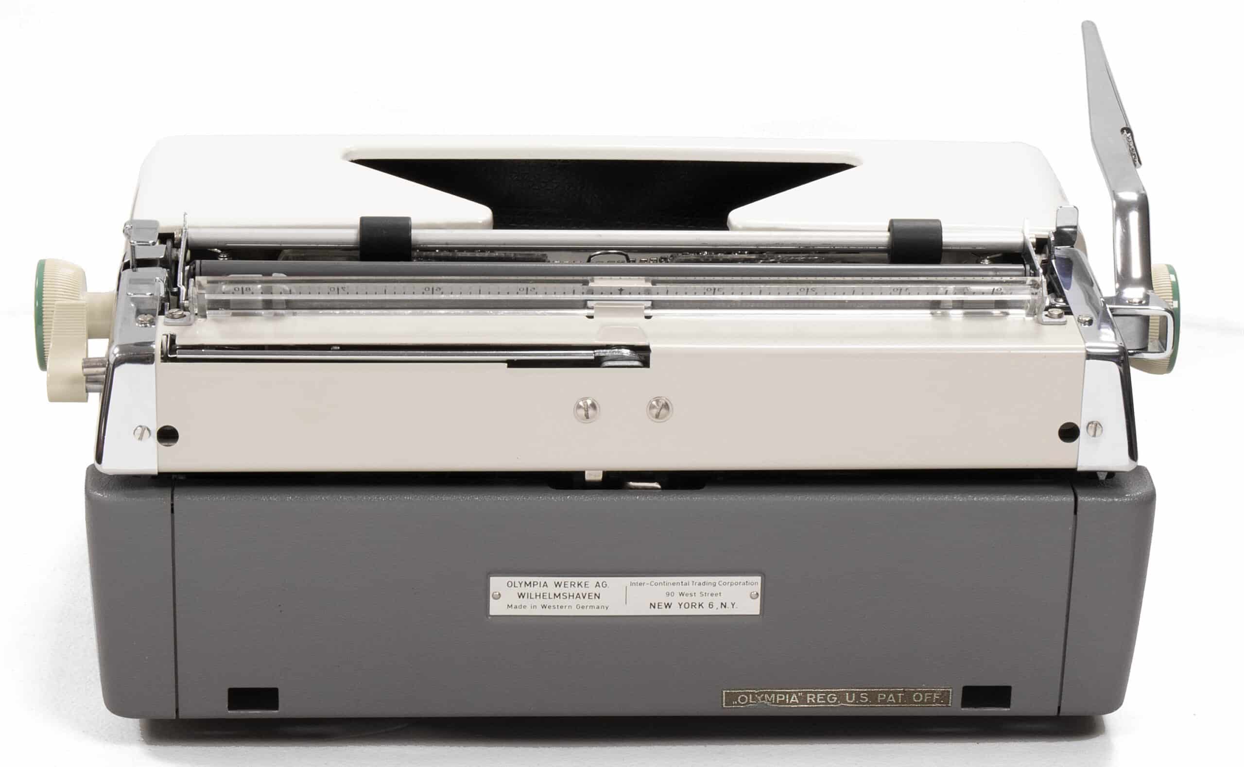 Rear view of a vintage Olympia typewriter with a gray metal body, exposed carriage rails, and a back manufacturer label.