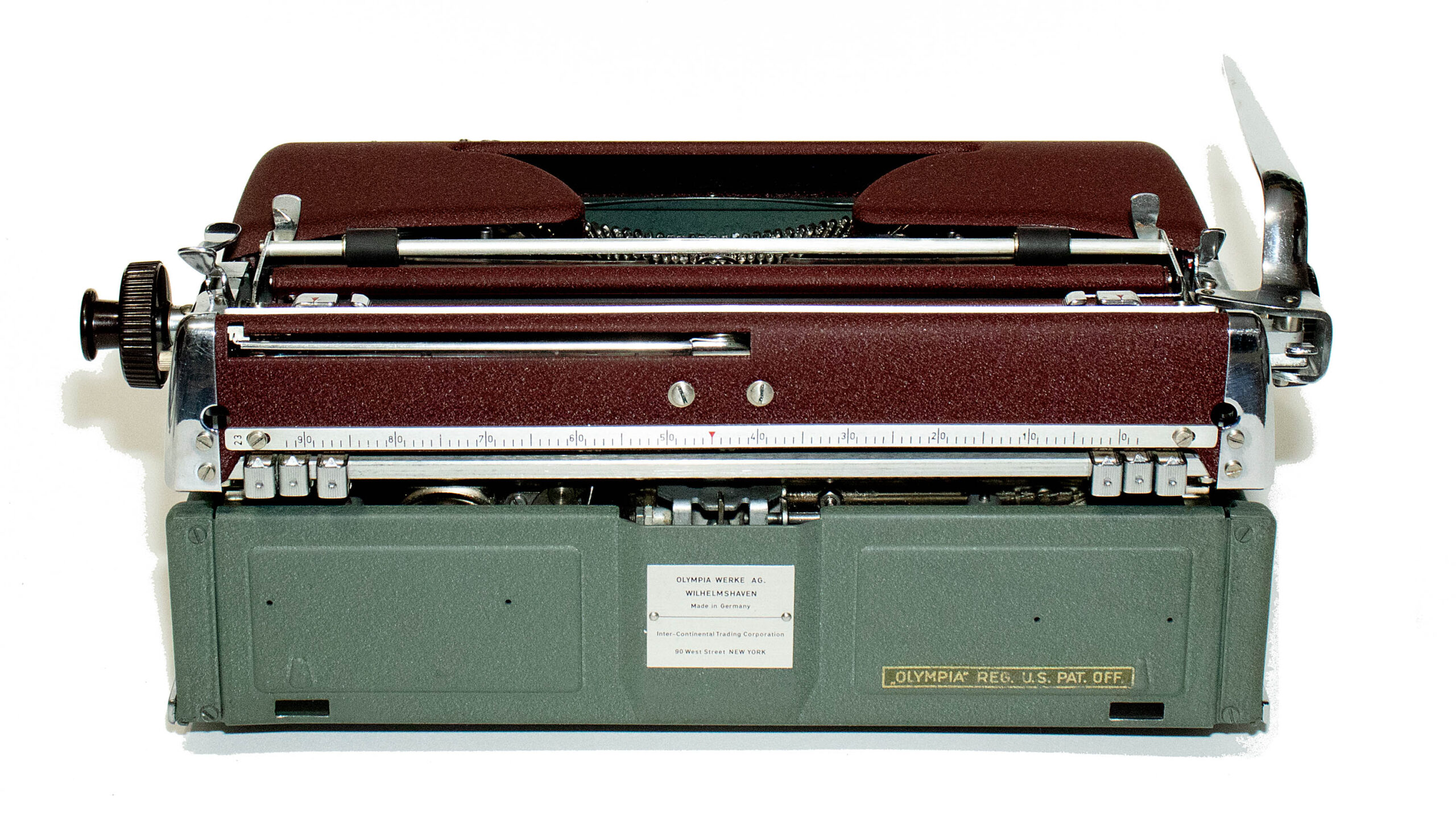 Vintage manual typewriter with brown case and metal carriage, showing a ruler-style front panel and brand plate reading Olympia Werke AG.