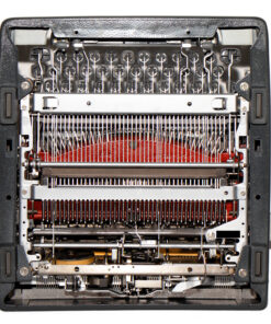Top-down view of an open vintage typewriter showing type bars, hammers, and a red ink ribbon railings across the middle.