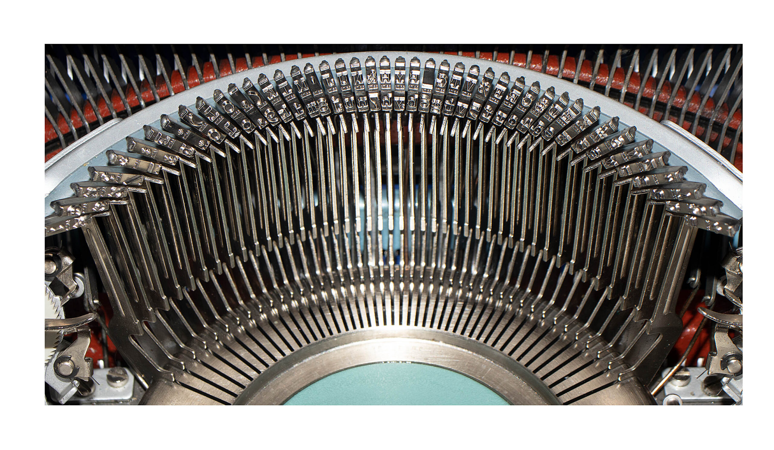 Close-up of a vintage typewriter showing metal type slug faces arranged in a curved arc around the typing area.