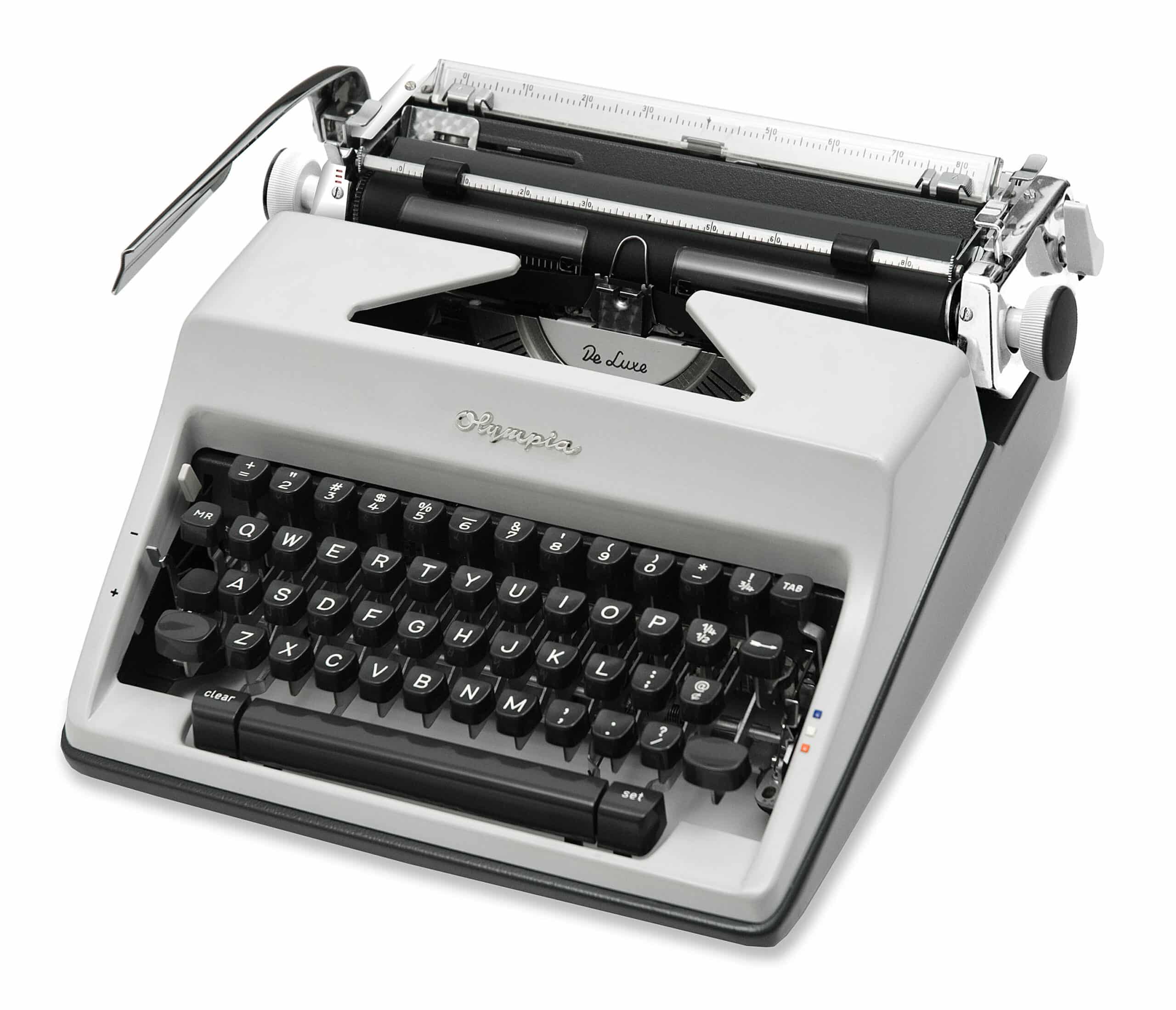 Close-up of a vintage gray manual typewriter showing the keyboard and metal carriage in a diagonal view, with 'De Luxe' lettering visible over the platen.