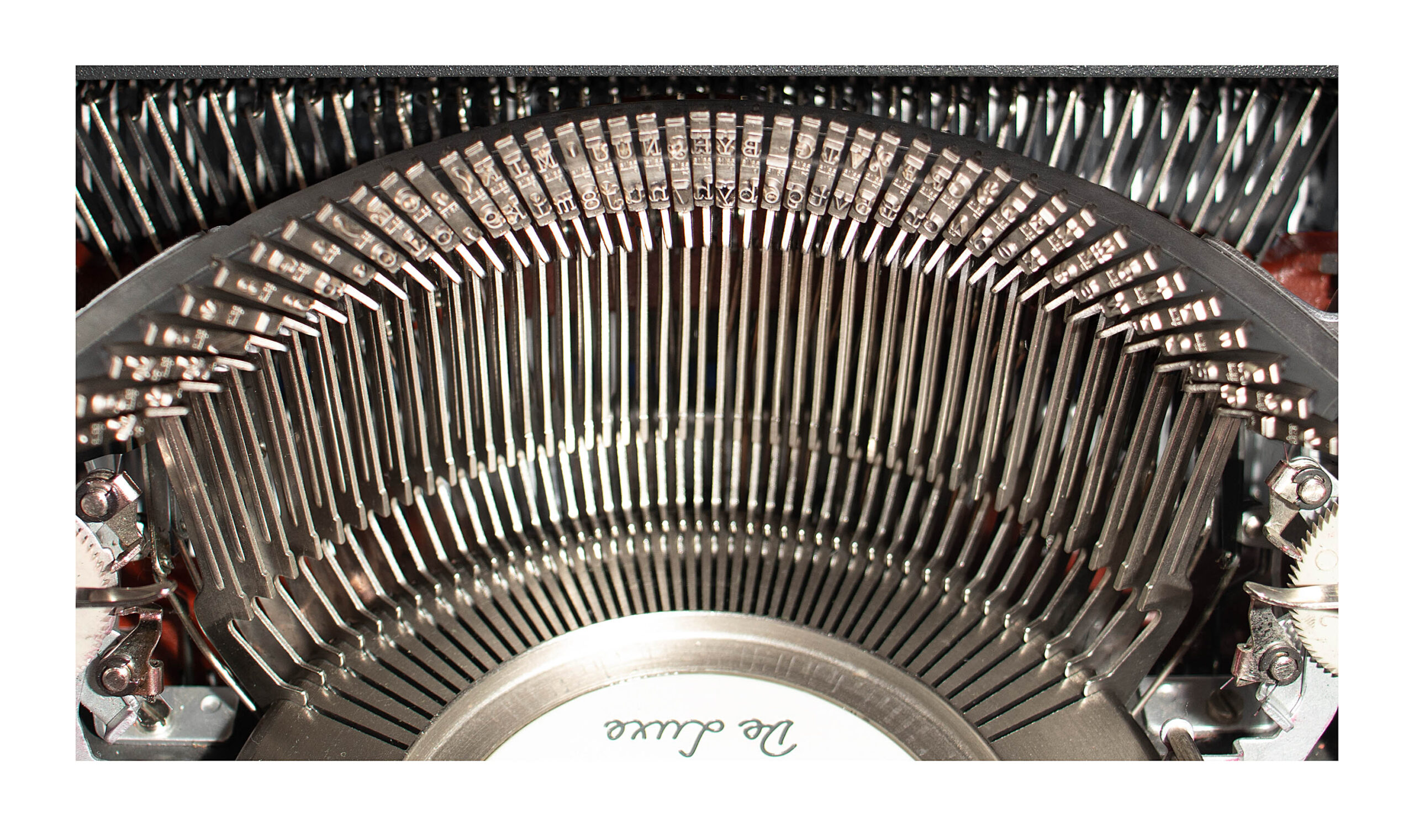 Macro view of a vintage typewriter’s inner type hammers arranged in a curved arc on the mechanism.