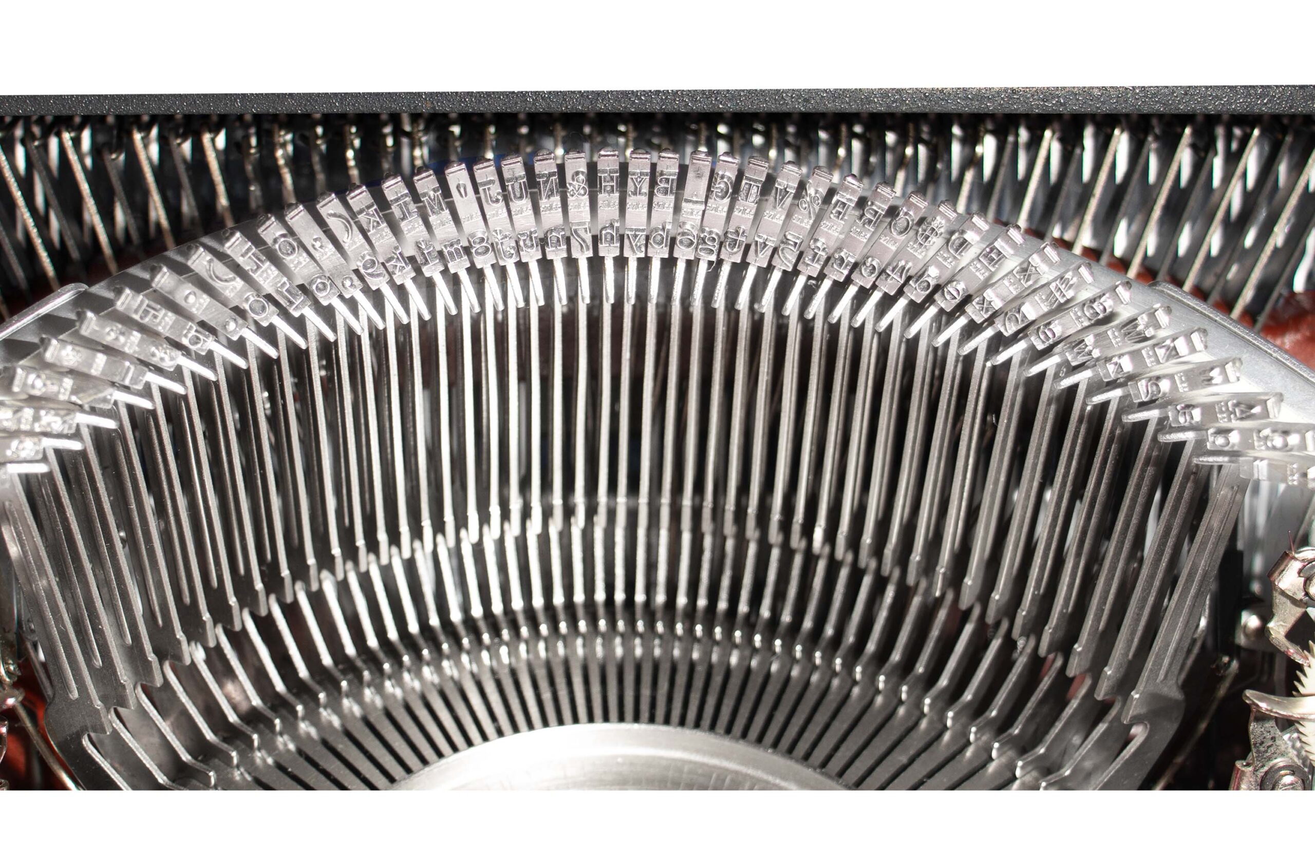 Close-up of a curved row of metal type slugs with letters, part of a vintage printer or typewriter mechanism