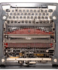 Close-up of a vintage typewriter's inner mechanism, showing keys, type bars, ribbon, and alignment wheels in metallic and gray tones.