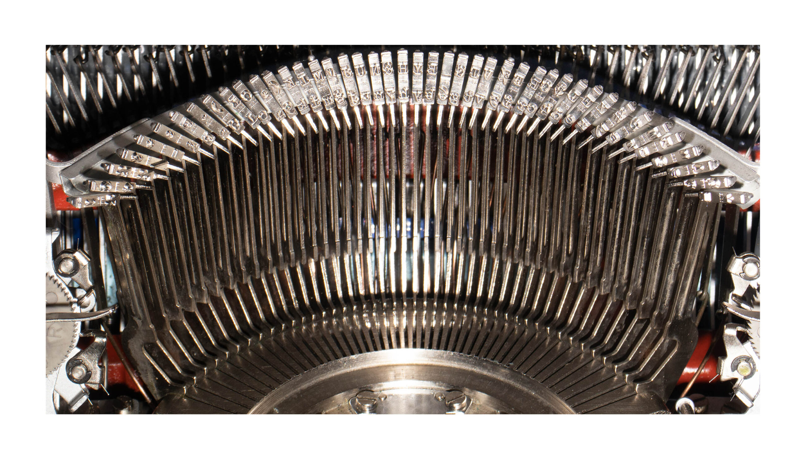 Close-up of a vintage typewriter's metal type bars and type slugs arranged in a curved arc.