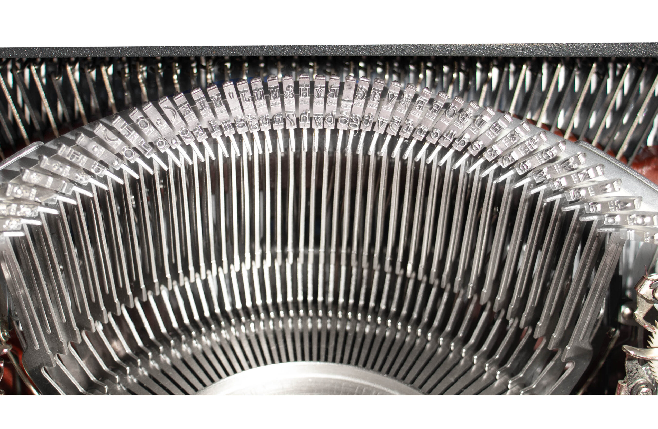 Close-up of metal type slugs arranged in a curved fan inside a vintage typewriter mechanism, showing rows of stamped letters.